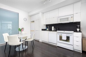 Cozinha moderna com armários brancos, micro-ondas, forno e área de refeições com mesa e cadeiras.