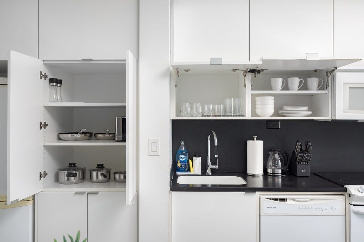 A modern kitchen with white cabinetry, a dishwasher, a sink, and various kitchen utensils.