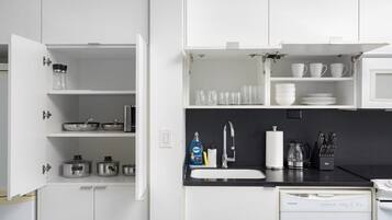 A modern kitchen with white cabinetry, a dishwasher, a sink, and various kitchen utensils.