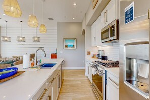 A modern kitchen with a central island, stainless steel appliances, pendant lighting, and a view of the outdoors. - Palmilla Beach Resort-136 Palmilla Circle Unit 301 (Port Aransas)