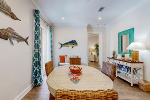 A dining area with a round table, wicker chairs, and a decorative fish wall hanging. - Palmilla Beach Resort-137 Palmilla Circle Unit 103 (Port Aransas)