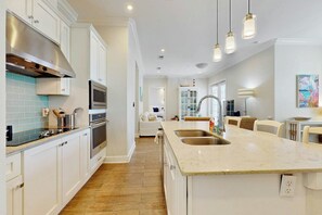 A modern kitchen with white cabinetry, a central island with a sink, and a dining area with a table and chairs. - Palmilla Beach Resort-137 Palmilla Circle Unit 104 (Port Aransas)