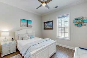A bedroom with a bed, a nightstand, a lamp, a ceiling fan, and artwork on the walls. - Palmilla Beach Resort-137 Palmilla Circle Unit 105 (Port Aransas)