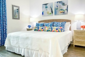 Ein Hotelzimmer mit einem großen Bett, zwei Nachttischen, einer Lampe, einer Vase mit Blumen und abstrakter Kunst an der Wand.