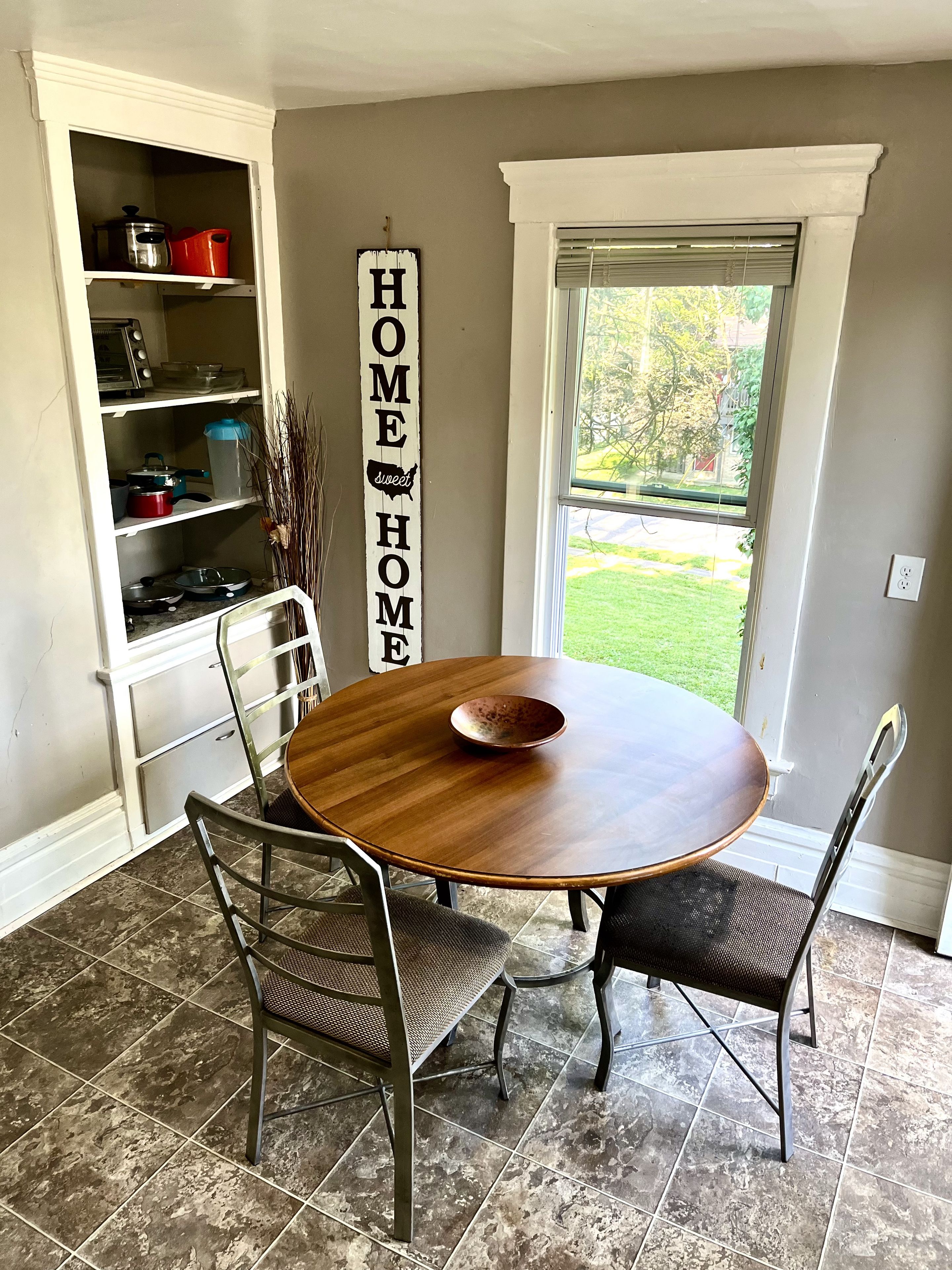 Un comedor con una mesa redonda, cuatro sillas y una estantería de cocina con diversos objetos.