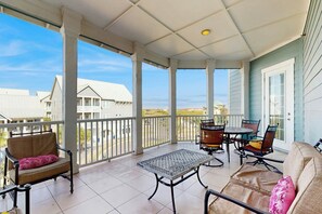 A covered outdoor area with a table and chairs, a sofa, and a view of buildings in the distance. - Palmilla Beach Resort-137 Palmilla Circle Unit 303 (Port Aransas)