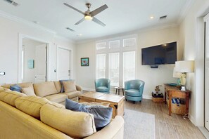 Ein Wohnzimmer mit einer Couch, Sesseln, einem Couchtisch, einem Fernseher und einem Deckenventilator.