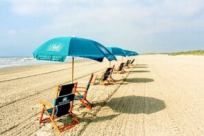 Ein Strand mit Reihen aus blauen Sonnenschirmen und Liegestühlen, der auf ein Resort hindeutet.