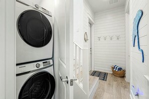 A laundry room with two stacked washers and dryers, a door leading to another room, a wall-mounted towel rack, and a woven basket with towels. - Palmilla Beach Resort-214 Sunset Avenue Casita 4 (Port Aransas)