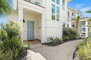 A white building with a blue door, a covered porch, and a brick pathway. - Palmilla Beach Resort-214 Sunset Avenue Casita 4 (Port Aransas)