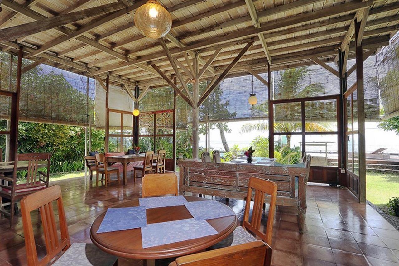 Een terras buiten met houten tafels en stoelen, een overdekt dak en uitzicht op zee.