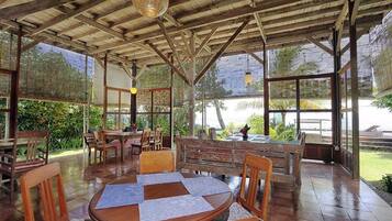 Een terras buiten met houten tafels en stoelen, een overdekt dak en uitzicht op zee.