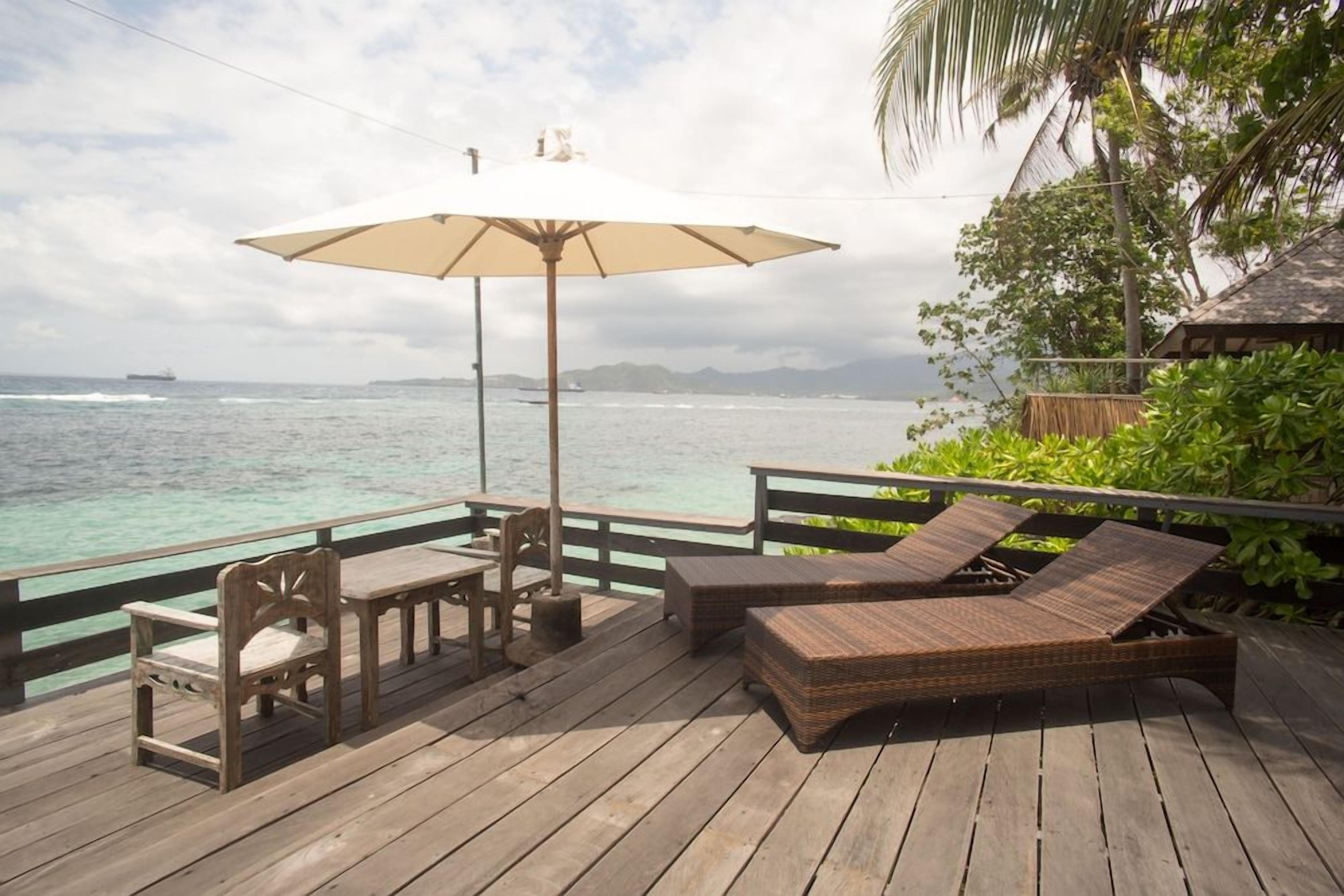 Een houten terras met een tafel, stoelen en een lounge fauteuil, plus een parasol.