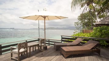 Een houten terras met een tafel, stoelen en een lounge fauteuil, plus een parasol.