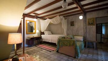 Een slaapkamer met een hemelbed, nachtkastje met lamp, spiegel en een houten bankje.