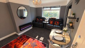 A modern living room with a fireplace, a dining area with a table set for two, and a large window providing natural light. - Unique 2 Floor Apartment in Manchester. Private Cinema! (Manchester)