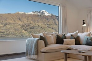 Ein Wohnzimmer mit einer Couch und einem Tisch, ein großes Fenster mit Blick auf die Berge und eine Wandlampe.