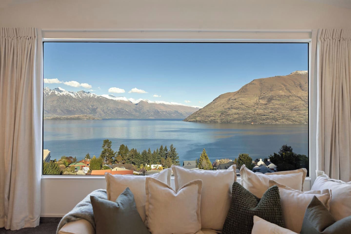 Ein Zimmer mit großem Fenster mit Blick auf einen See und Berge.