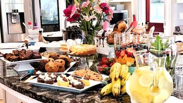 A kitchen counter with a variety of food items, including pastries, fruits, and a pitcher of lemonade.