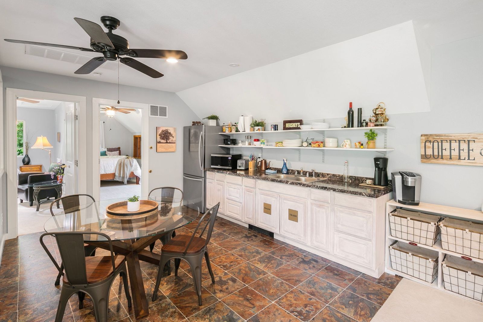 A modern kitchen with white cabinets, a granite countertop, and a dining area with a glass table and chairs.