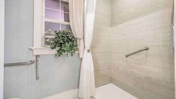 A bathroom with a shower, a window with a birdcage and plants, and a handrail.