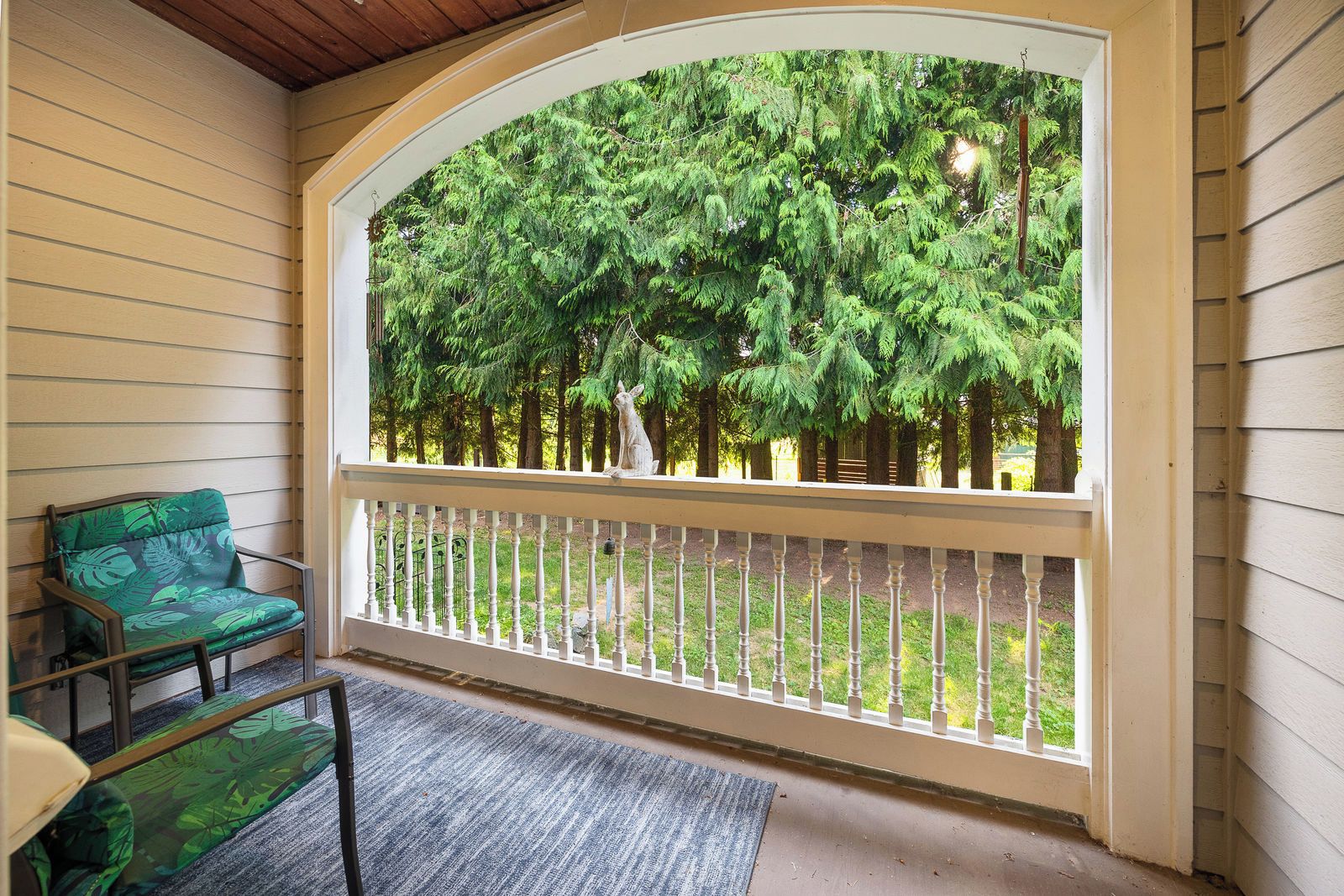 A porch with a view of a forest, a chair, and a railing.