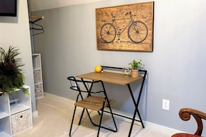 Una habitación compacta con un pequeño escritorio de madera, dos sillas, una planta en maceta y una obra de arte de una bicicleta colgada en la pared.
