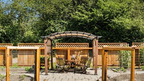 Un patio jardín con una pérgola de madera, una mesa con sillas y un área cercada donde se ve el número '302'.