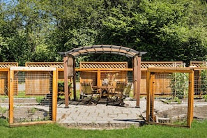 A garden patio with a wooden pergola, a table with chairs, and a fenced area with a number '302' visible. - The Grayson B&B Extended Stays (Monroe)