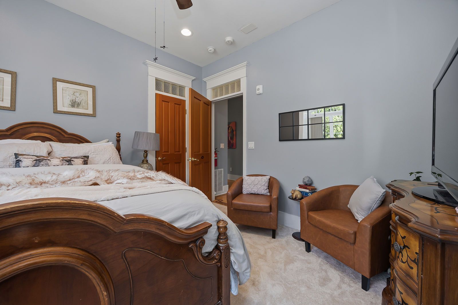 A bedroom with a large bed, two chairs, a dresser, and a television.
