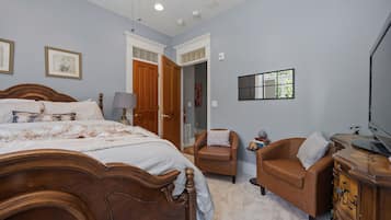 A bedroom with a large bed, two chairs, a dresser, and a television.