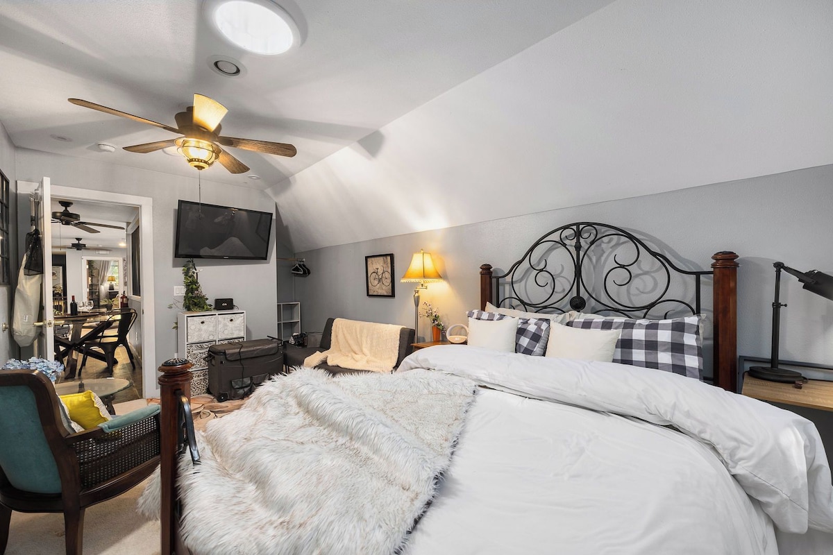 A bedroom with a bed, a ceiling fan, a TV, a desk, and a chair.