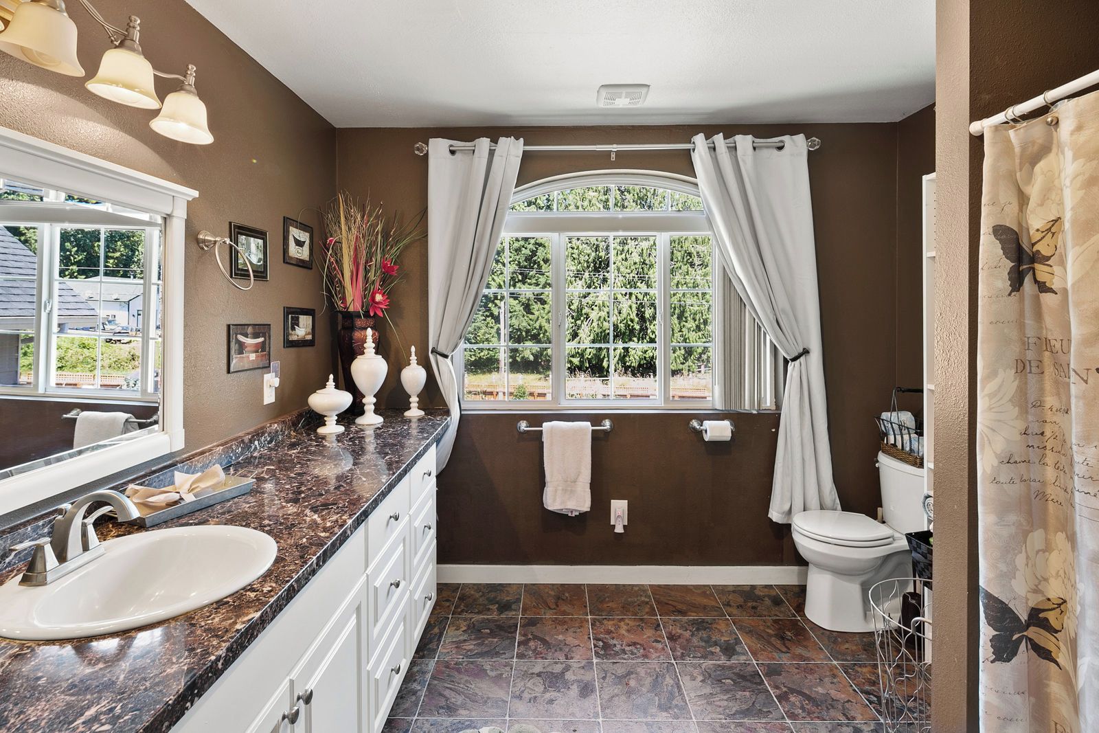 A bathroom with a marble countertop, a white sink, a toilet, and a window with curtains.
