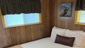 Une chambre à coucher avec un lit, une fenêtre avec des stores, un tableau accroché au mur et un rideau.