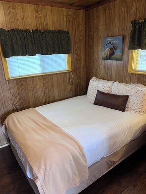 A bedroom with a bed, a window with blinds, a wall-mounted painting, and a curtain.