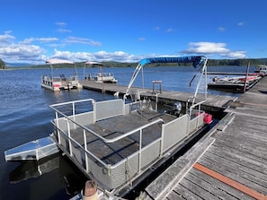 Une jetée avec un bateau, un espace de repos abrité et une vue sur un lac, avec des montagnes en arrière-plan.