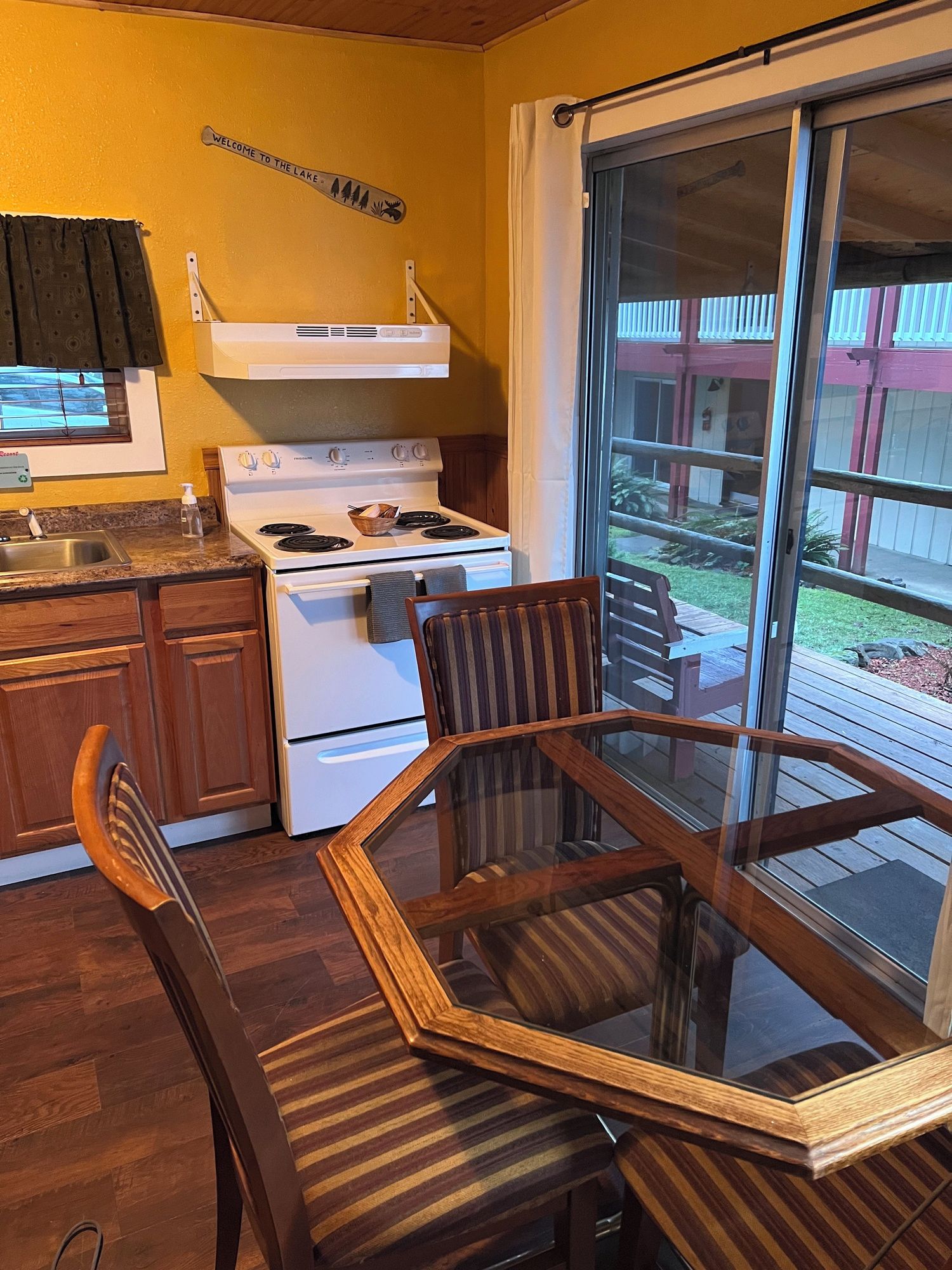 A kitchen with a stove, sink, and a dining area with a glass table and chairs.