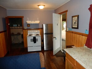 A compact kitchen with a stove, oven, and refrigerator, wooden paneling, and a door leading outside.