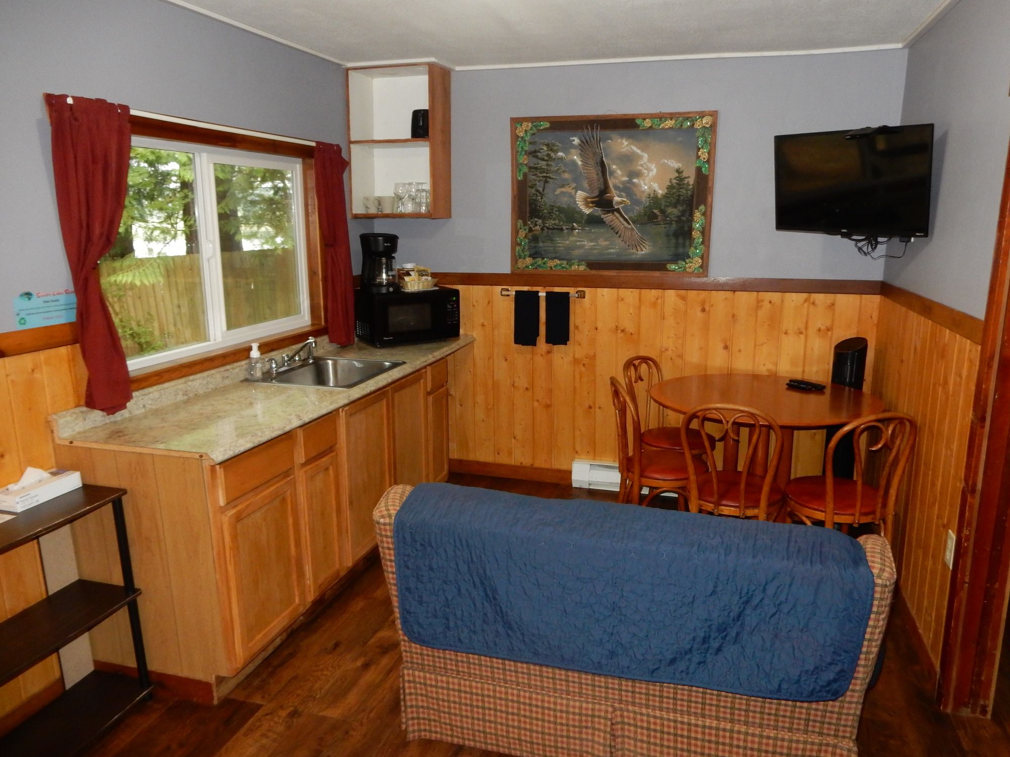 A compact kitchen with a sink, a microwave, and a coffee maker. There is a dining area with a table and chairs, and a television mounted on the wall.