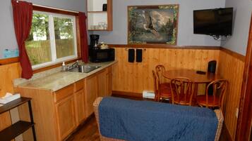 A compact kitchen with a sink, a microwave, and a coffee maker. There is a dining area with a table and chairs, and a television mounted on the wall.