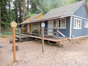 A rustic cabin with a porch, wooden steps, and a gravel ground.