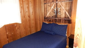 Una habitación de madera con una cama, un adorno en la pared y una mesita.