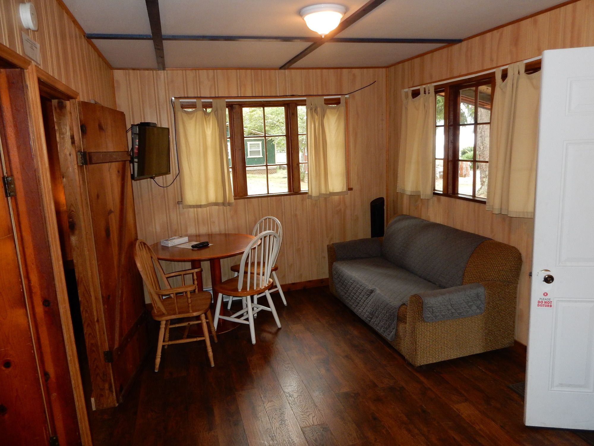A room with wooden walls, a sofa, a table with chairs, and a television mounted on the wall.