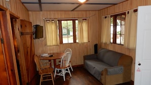Una habitación con paredes de madera, un sofá, una mesa con sillas y un televisor montado en la pared.