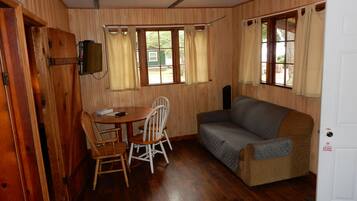 A room with wooden walls, a sofa, a table with chairs, and a television mounted on the wall.