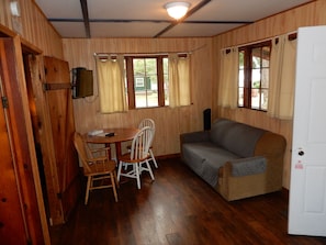 A room with wooden walls, a sofa, a table with chairs, and a television mounted on the wall. - Cabin 9: A Comfortable Two-Bedroom Cabin by Silver Lake (Silver Lake)