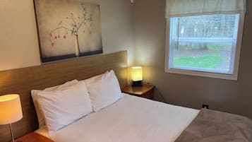 Een hotelkamer met een bed, een bedlamp, een nachtkastje, een schilderij aan de muur en een raam met jaloezieën.