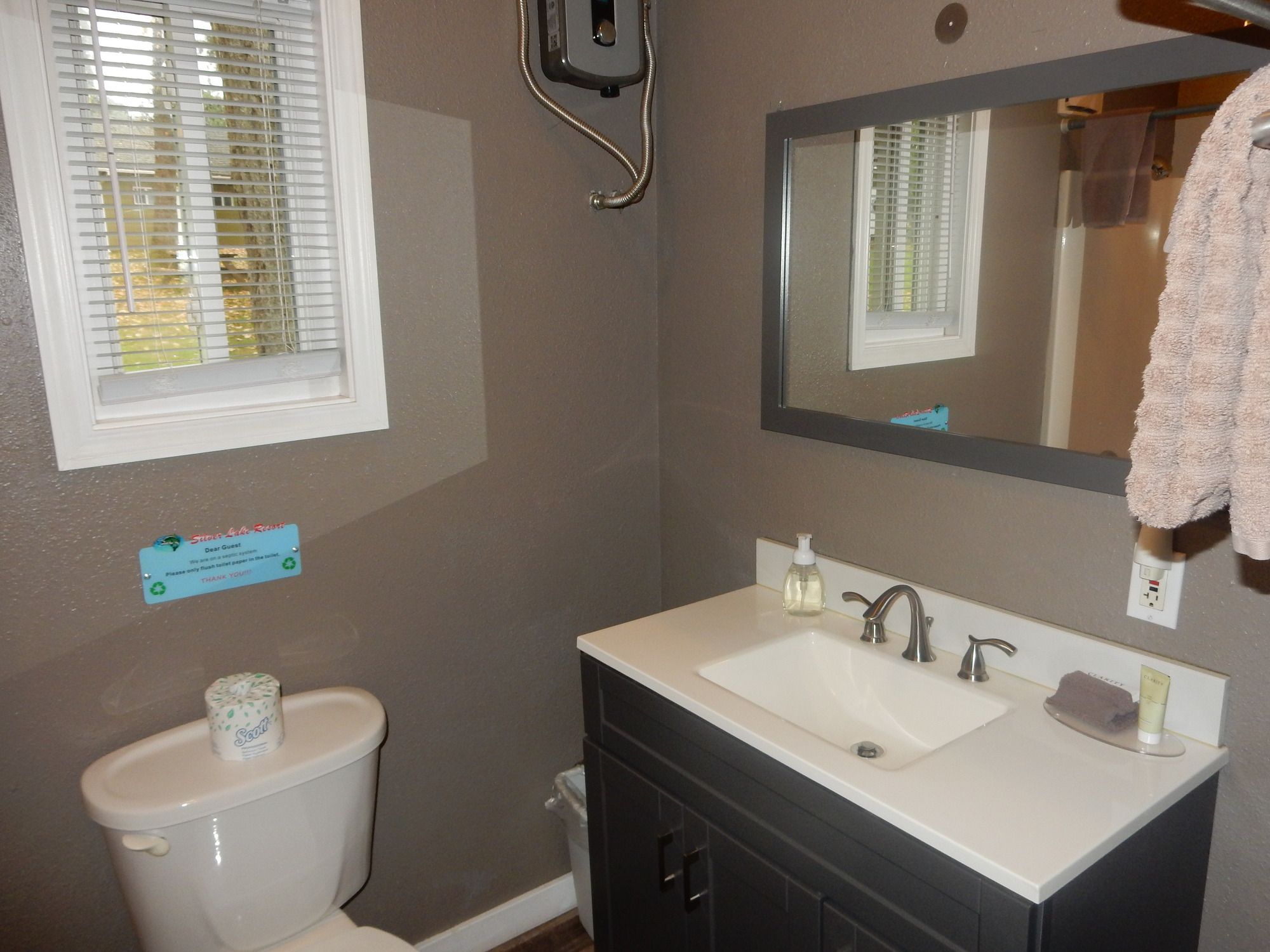 A bathroom with a toilet, sink, mirror, and a window with blinds.
