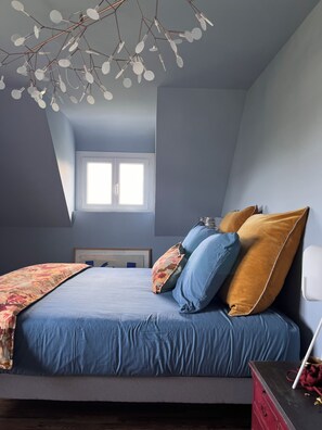 Ein Schlafzimmer mit einem Bett, Kissen, einem Nachttisch, einer Kommode, einem Fenster und einer Deckenleuchte.