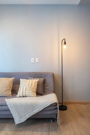 Ein modernes Wohnzimmer mit einem grauen Sofa, zwei Kissen, einer Decke und einer Stehlampe.